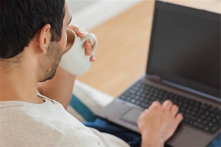 simsearch:6109-08581996,k - Handsome brown haired man drinking coffee while using his laptop in bright living room Fotografie stock - Microstock e Abbonamento, Codice: 400-07058752