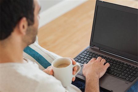 simsearch:6109-08581996,k - Brown haired man holding coffee using his laptop in bright living room Fotografie stock - Microstock e Abbonamento, Codice: 400-07058753