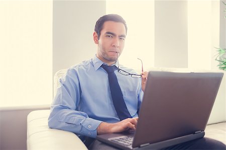 simsearch:400-07274613,k - Nervous man biting his eyeglasses and using a laptop sitting on a sofa Stock Photo - Budget Royalty-Free & Subscription, Code: 400-07058804