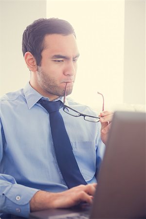 simsearch:400-07274613,k - Focused man biting his eyeglasses and using a laptop sitting on a sofa Stock Photo - Budget Royalty-Free & Subscription, Code: 400-07058802