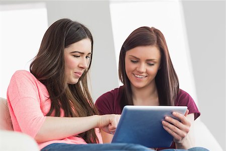simsearch:400-07059986,k - Two happy teenage girls sitting on a sofa using a tablet pc in a living room Stock Photo - Budget Royalty-Free & Subscription, Code: 400-07058991
