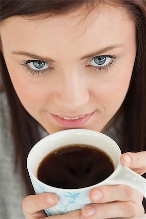 simsearch:400-06932687,k - Smiling brunette drinking a cup of coffee looking at camera Stock Photo - Budget Royalty-Free & Subscription, Code: 400-07059049