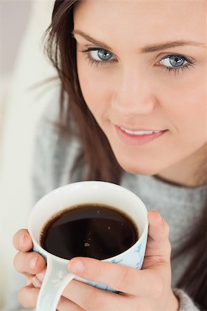 simsearch:400-06932687,k - Happy brunette holding a cup of coffee looking at camera Stock Photo - Budget Royalty-Free & Subscription, Code: 400-07059050