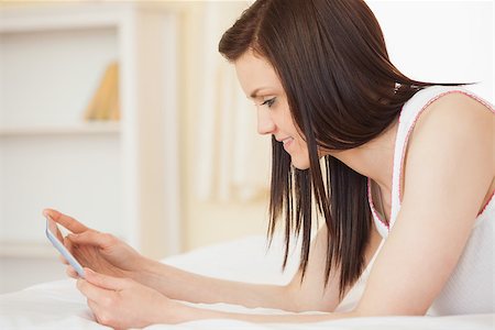 simsearch:400-06932687,k - Smiling brunette using a tablet pc lying on her bed in a bedroom Stock Photo - Budget Royalty-Free & Subscription, Code: 400-07059082