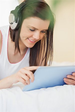 simsearch:400-06932687,k - Happy girl listening to music with a headset and using a tablet pc lying on a bed in a bedroom Stock Photo - Budget Royalty-Free & Subscription, Code: 400-07059094