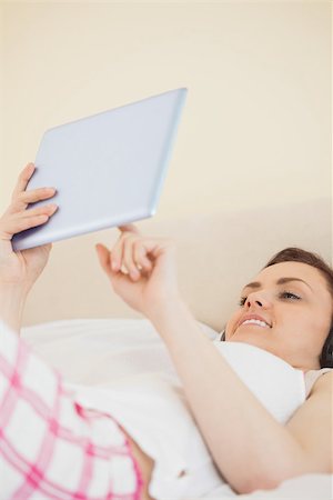 simsearch:400-06932687,k - Smiling brunette holding a tablet pc lying on a bed in a bedroom Stock Photo - Budget Royalty-Free & Subscription, Code: 400-07059097