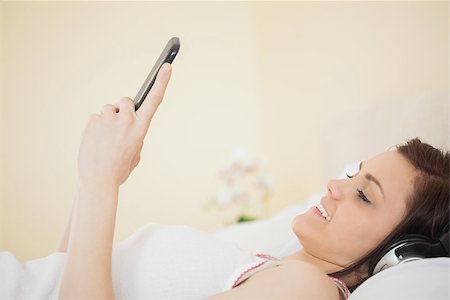 simsearch:400-06932687,k - Smiling girl listening music on her smartphone lying on bed in a bedroom Stock Photo - Budget Royalty-Free & Subscription, Code: 400-07059100