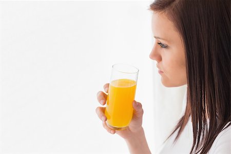 simsearch:400-06932687,k - Thoughtful brunette holding a glass of orange juice and looking away on white background Stock Photo - Budget Royalty-Free & Subscription, Code: 400-07059117