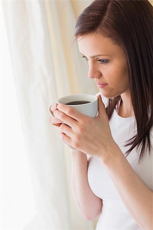 simsearch:400-06932687,k - Thoughtful brunette holding a cup of coffee and looking away in a bedroom Stock Photo - Budget Royalty-Free & Subscription, Code: 400-07059113