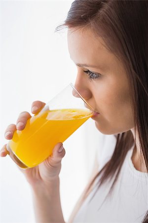 simsearch:400-06932687,k - Relaxed brunette drinking a glass of orange juice on white background Stock Photo - Budget Royalty-Free & Subscription, Code: 400-07059123