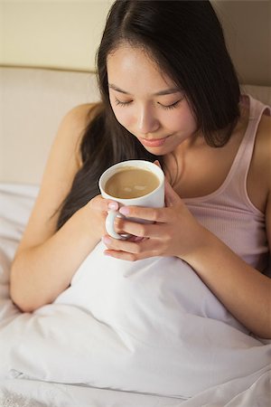 simsearch:6109-08489191,k - Cheerful young asian woman sitting in bed smelling her morning coffee at home in bedroom Fotografie stock - Microstock e Abbonamento, Codice: 400-07060679