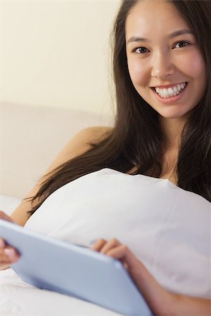 Pretty young asian woman sitting in bed using her digital tablet smiling at camera at home in bedroom Stock Photo - Budget Royalty-Free & Subscription, Code: 400-07060671