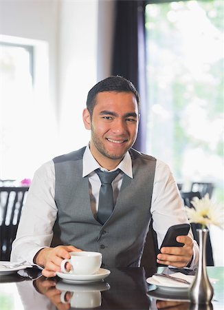 simsearch:400-07137867,k - Smiling businessman having coffee and holding phone looking at camera Fotografie stock - Microstock e Abbonamento, Codice: 400-07060746