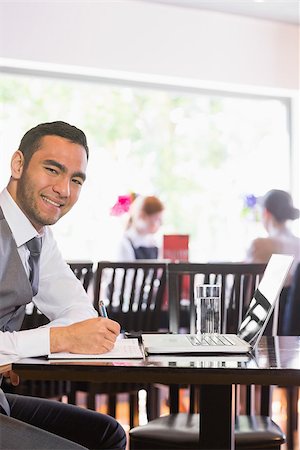 simsearch:400-07137867,k - Happy businessman writing while smiling at camera in a restaurant Fotografie stock - Microstock e Abbonamento, Codice: 400-07060790