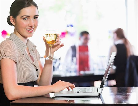 simsearch:400-07137867,k - Happy businesswoman holding wine glass using laptop and looking at camera in a restaurant Fotografie stock - Microstock e Abbonamento, Codice: 400-07060809