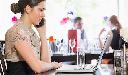 simsearch:400-07137867,k - Businesswoman calling on phone while looking at laptop screen in a restaurant Fotografie stock - Microstock e Abbonamento, Codice: 400-07060817