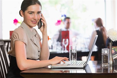 simsearch:400-07137867,k - Businesswoman calling on phone using laptop looking at camera in a cafe Fotografie stock - Microstock e Abbonamento, Codice: 400-07060820