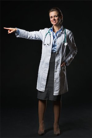 simsearch:400-07099882,k - Full length portrait of smiling doctor woman pointing on copy space isolated on black Photographie de stock - Aubaine LD & Abonnement, Code: 400-07099874