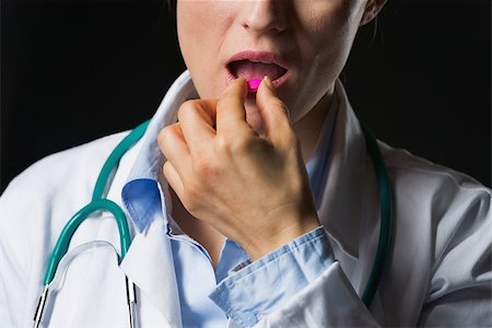 simsearch:400-04130714,k - Closeup on doctor woman eating pill isolated on black Photographie de stock - Aubaine LD & Abonnement, Code: 400-07099877