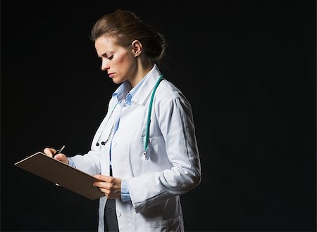 simsearch:400-07099882,k - Serious doctor woman writing in clipboard isolated on black Photographie de stock - Aubaine LD & Abonnement, Code: 400-07099881