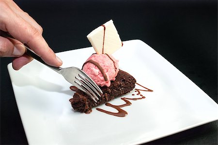 Close-up of a man's hand using a fork to get a taste of brownie with raspberry icecream and a white chocolate garnish. Stock Photo - Budget Royalty-Free & Subscription, Code: 400-07114997