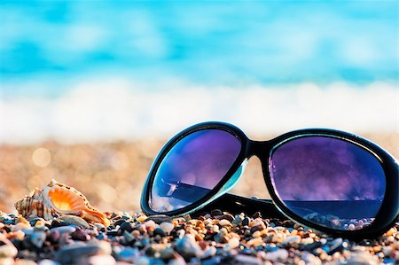 simsearch:400-04241229,k - Sunglasses and shells lie on the shingle beach sea Fotografie stock - Microstock e Abbonamento, Codice: 400-07124091