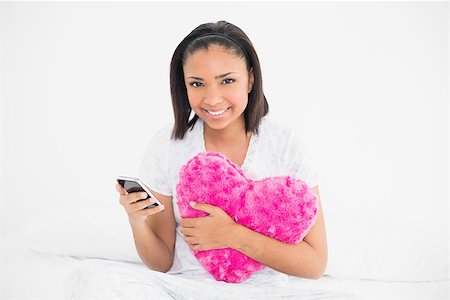 simsearch:400-07127238,k - Delighted young dark haired model holding a pillow and a mobile phone in bright bedroom Foto de stock - Royalty-Free Super Valor e Assinatura, Número: 400-07127214