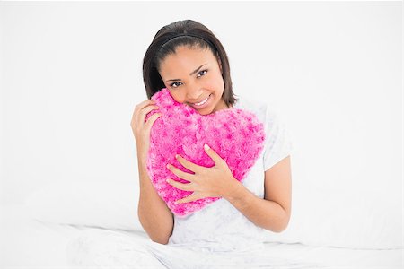 simsearch:400-07127238,k - Amused young dark haired model cuddling a heart-shaped pillow in bright bedroom Foto de stock - Royalty-Free Super Valor e Assinatura, Número: 400-07127210