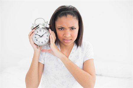simsearch:400-07127238,k - Frowning young dark haired model holding an alarm clock in bright bedroom Foto de stock - Royalty-Free Super Valor e Assinatura, Número: 400-07127273