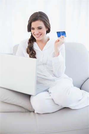 simsearch:400-07474252,k - Laughing casual brown haired woman in white pajamas shopping online with her laptop in a bright living room Stock Photo - Budget Royalty-Free & Subscription, Code: 400-07127873