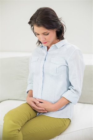 Calm pregnant brown haired woman holding her belly in a bright living room Stock Photo - Budget Royalty-Free & Subscription, Code: 400-07128652