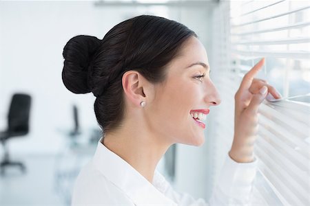 Close up side view of a smiling young business woman peeking through blinds at office Stock Photo - Budget Royalty-Free & Subscription, Code: 400-07134332