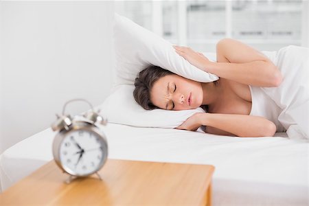 Young woman covering ears with pillow in bed and alarm clock on side table Stock Photo - Budget Royalty-Free & Subscription, Code: 400-07134743
