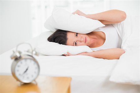 Young woman covering ears with pillow in bed and alarm clock on side table Stock Photo - Budget Royalty-Free & Subscription, Code: 400-07135246