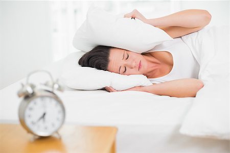 Young woman covering ears with pillow in bed and alarm clock on side table Stock Photo - Budget Royalty-Free & Subscription, Code: 400-07135248