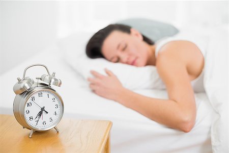 Blurred young woman sleeping in bed with alarm clock on bedside table in bedroom Stock Photo - Budget Royalty-Free & Subscription, Code: 400-07135240