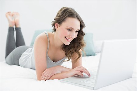 Smiling casual young brunette using laptop in bed at home Stock Photo - Budget Royalty-Free & Subscription, Code: 400-07136424