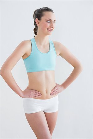 simsearch:400-07136501,k - Smiling toned young woman with hands on hips against wall in fitness studio Photographie de stock - Aubaine LD & Abonnement, Code: 400-07136494