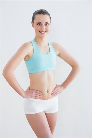 simsearch:400-07136501,k - Portrait of a smiling toned young woman with hands on hips against wall in fitness studio Photographie de stock - Aubaine LD & Abonnement, Code: 400-07136493
