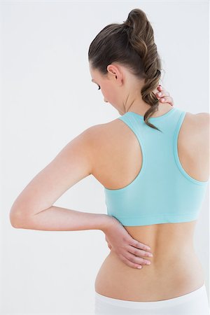 simsearch:400-07136501,k - Rear view of a toned young woman with back pain standing against wall in fitness studio Photographie de stock - Aubaine LD & Abonnement, Code: 400-07136501