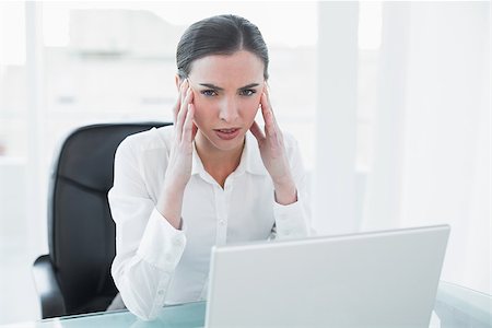 Portrait of a young businesswoman suffering from headache in front of laptop at office desk Stock Photo - Budget Royalty-Free & Subscription, Code: 400-07136938