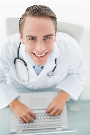 simsearch:695-05771285,k - Overhead portrait of a smiling male doctor using laptop at medical office Foto de stock - Royalty-Free Super Valor e Assinatura, Número: 400-07136990