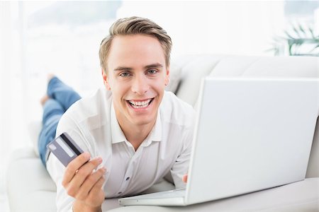 simsearch:6109-08395848,k - Cheerful casual young man doing online shopping through laptop and credit card on sofa Fotografie stock - Microstock e Abbonamento, Codice: 400-07137246