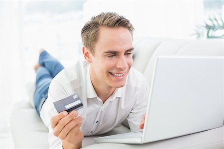 simsearch:6109-08395848,k - Cheerful casual young man doing online shopping through laptop and credit card on sofa Fotografie stock - Microstock e Abbonamento, Codice: 400-07137247