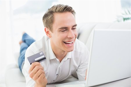 simsearch:6109-08395848,k - Cheerful casual young man doing online shopping through laptop and credit card on sofa Fotografie stock - Microstock e Abbonamento, Codice: 400-07137248