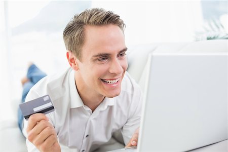 simsearch:6109-08395848,k - Cheerful casual young man doing online shopping through laptop and credit card on sofa Fotografie stock - Microstock e Abbonamento, Codice: 400-07137249