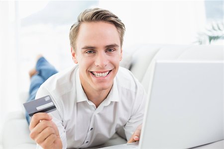simsearch:400-07268814,k - Cheerful casual young man doing online shopping through laptop and credit card on sofa Foto de stock - Royalty-Free Super Valor e Assinatura, Número: 400-07137250