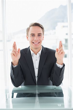 dedos cruzados - Portrait of a smiling young businessman with fingers crossed sitting at office desk Foto de stock - Super Valor sin royalties y Suscripción, Código: 400-07137284