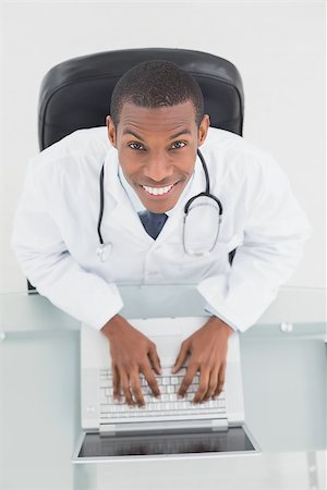 simsearch:695-05771285,k - Overhead portrait of a smiling male doctor using laptop at medical office Foto de stock - Royalty-Free Super Valor e Assinatura, Número: 400-07137537