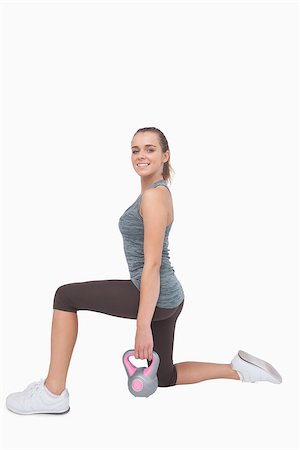 simsearch:400-07138263,k - Cheerful woman lunging and using a kettle bell smiling at camera Stock Photo - Budget Royalty-Free & Subscription, Code: 400-07138195